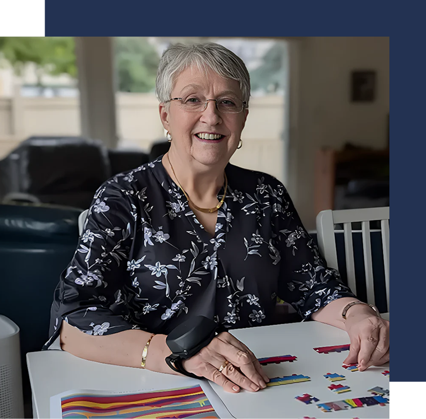 An older woman wearing tremor gloves while completing a tabletop puzzle to support steady hand movement.