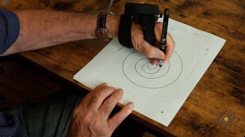 Man drawing a spiral at a table while wearing the Steadi-3 Plus on his hand