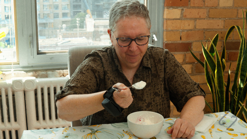 Woman eating with a spoon at home while wearing the Steadi-3 Plus on her hand