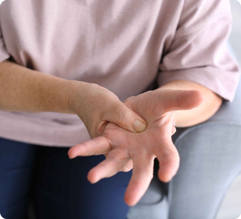 Person gripping their own trembling hand at the wrist, illustrating a common self-management technique for Parkinson's Disease hand tremors at work.
