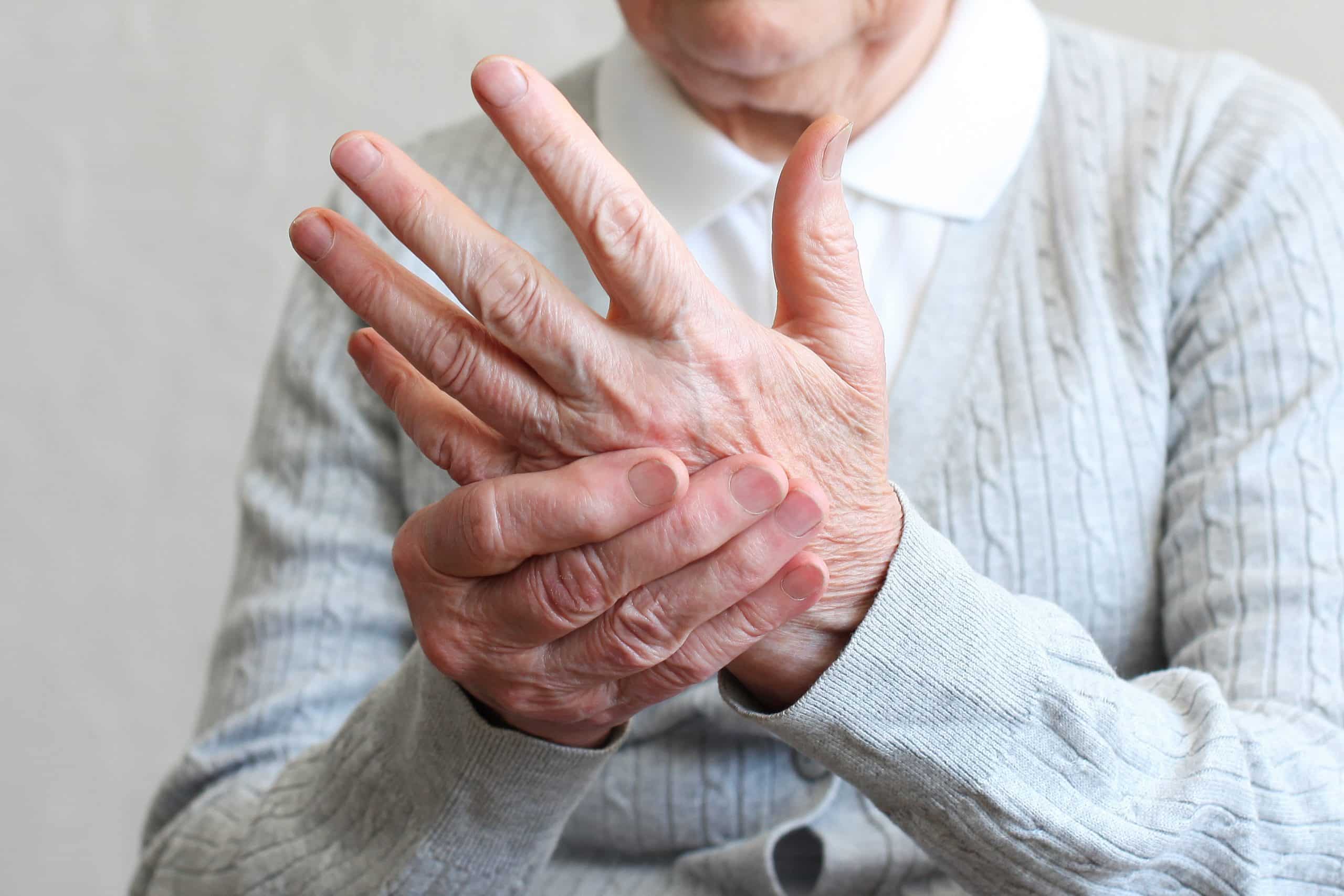 Elderly woman holding her hand, experiencing finger tremors.