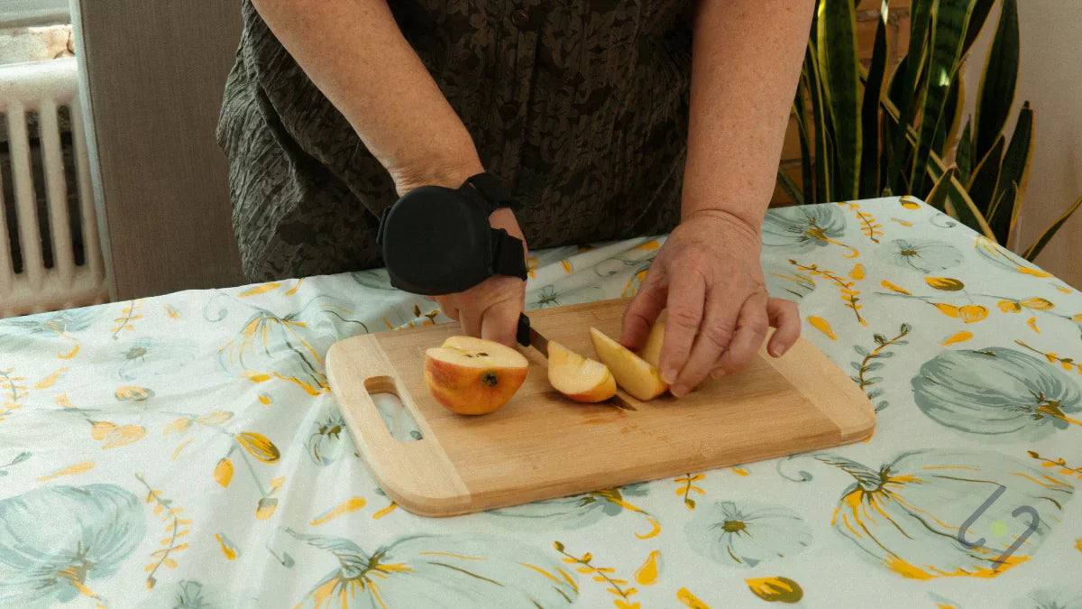 Person wearing Steadi-3 tremor glove while cutting fruit on board, improving hand control and safety during food preparation with Parkinson’s.