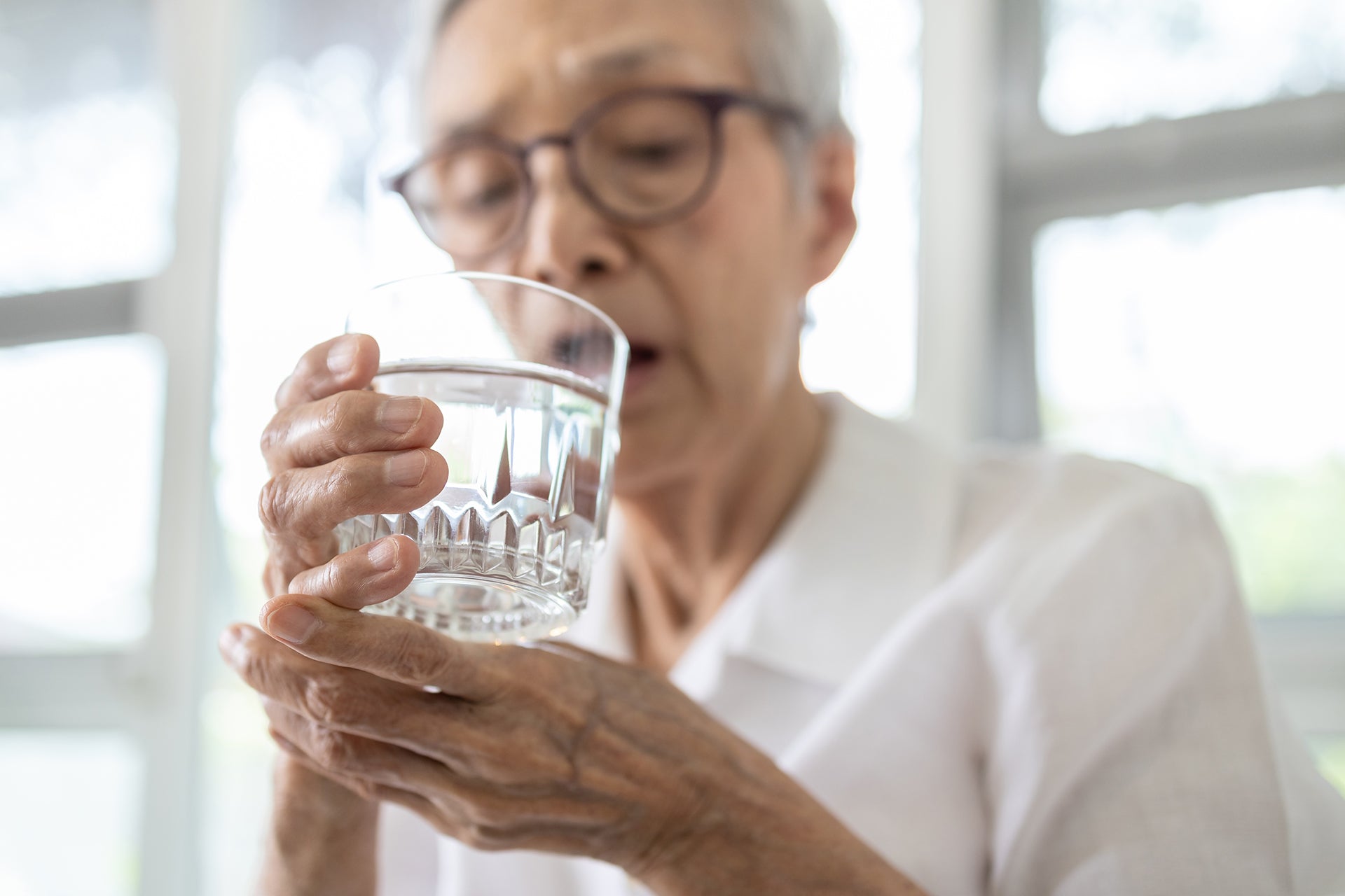  Elderly woman having difficulty drinking water due to her Parkinson's tremors.