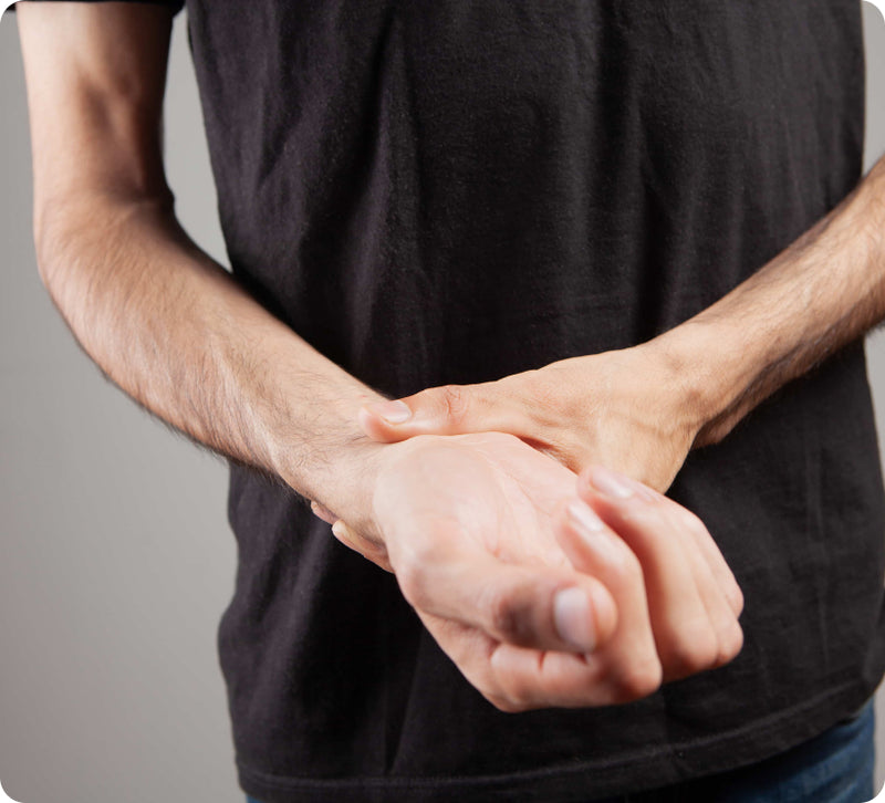 A close-up of a person's hands cramping or holding each other, wearing a black t-shirt against a neutral gray background.