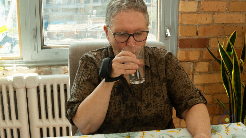 Woman sipping from a glass while wearing the Steadi-3 glove to help manage hand tremors.