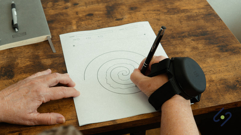 Woman drawing a spiral with a pen while wearing the Steadi-3 Plus