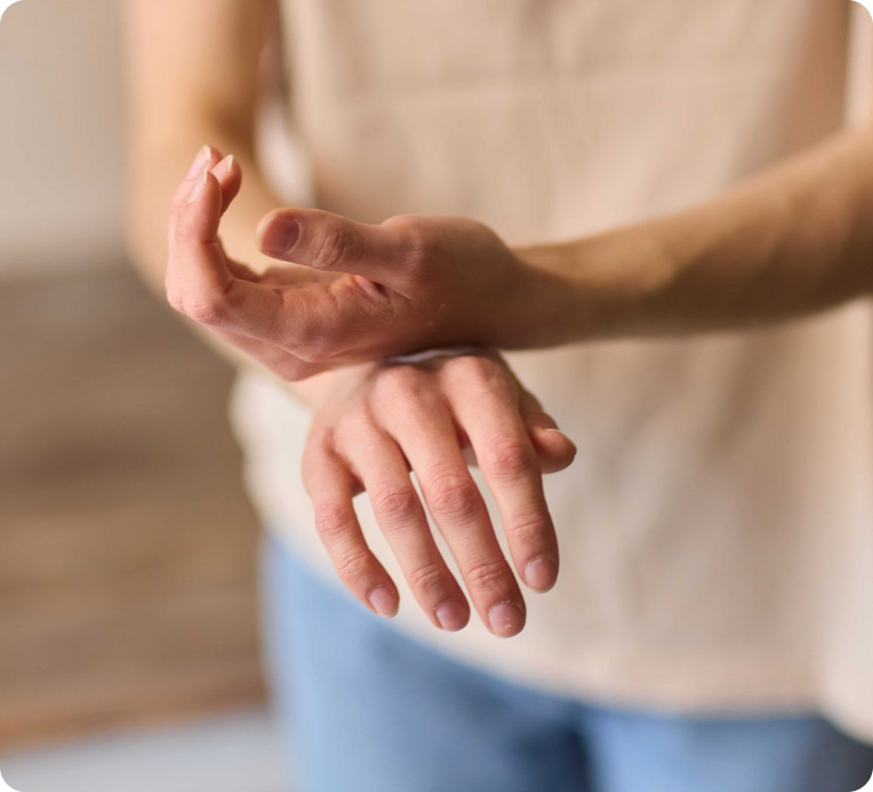 Close-up of a person's hands and wrists wearing a beige wristband or bracelet on one wrist, with a soft-focus indoor background.