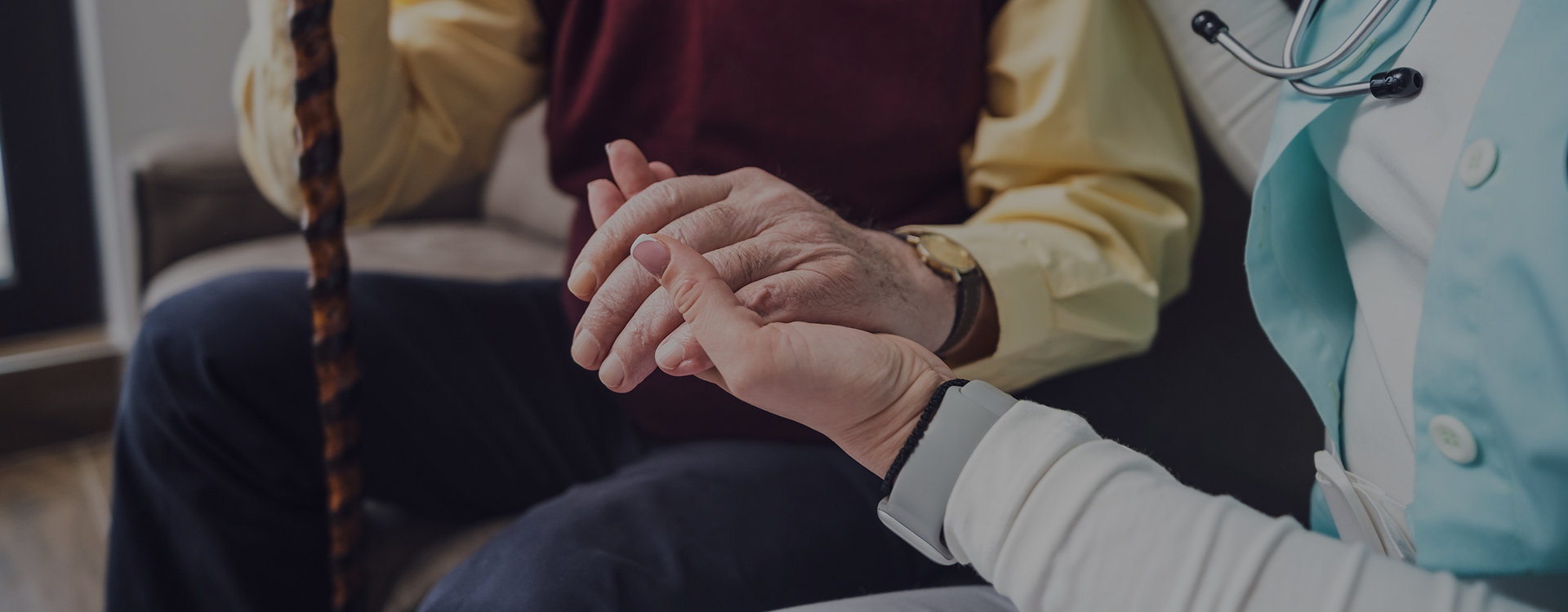 Healthcare professional holding the clasped hands of a patient with Parkinson's Disease, representing clinical support and staying employed.